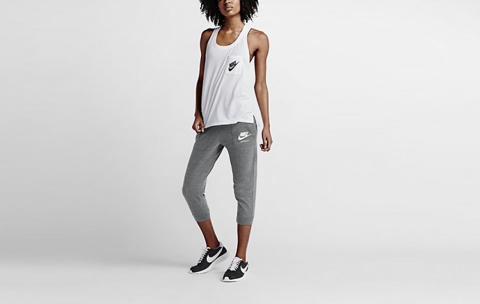 A woman wearing a white Nike tank, black running shoes and cropped grey sweatpants